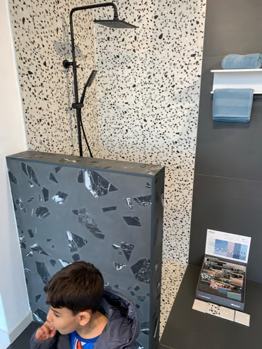 Mur en terrazzo, colonne de douche noire et finitions soignées.