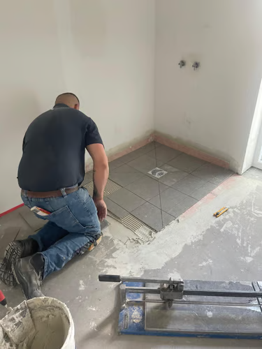 Préparation et pose de carrelage sur chape dans une salle d'eau en rénovation.
